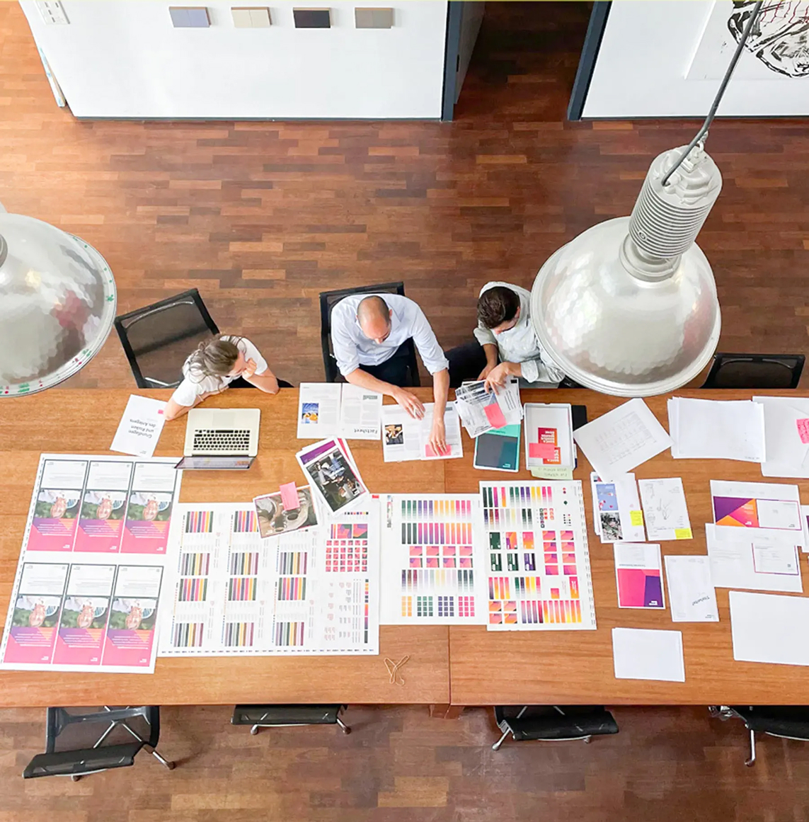 Blick von oben auf einen Arbeitstisch mit Layouts und dem Team
